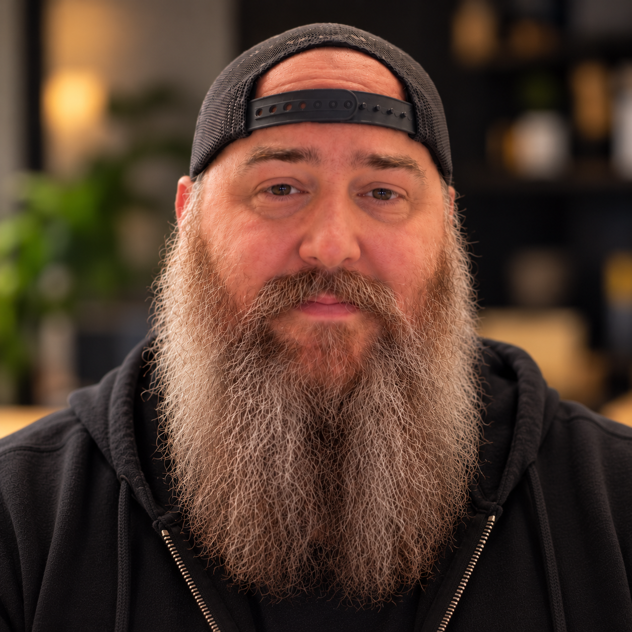 Justin wearing a backwards cap and a black hoodie, with a long beard
